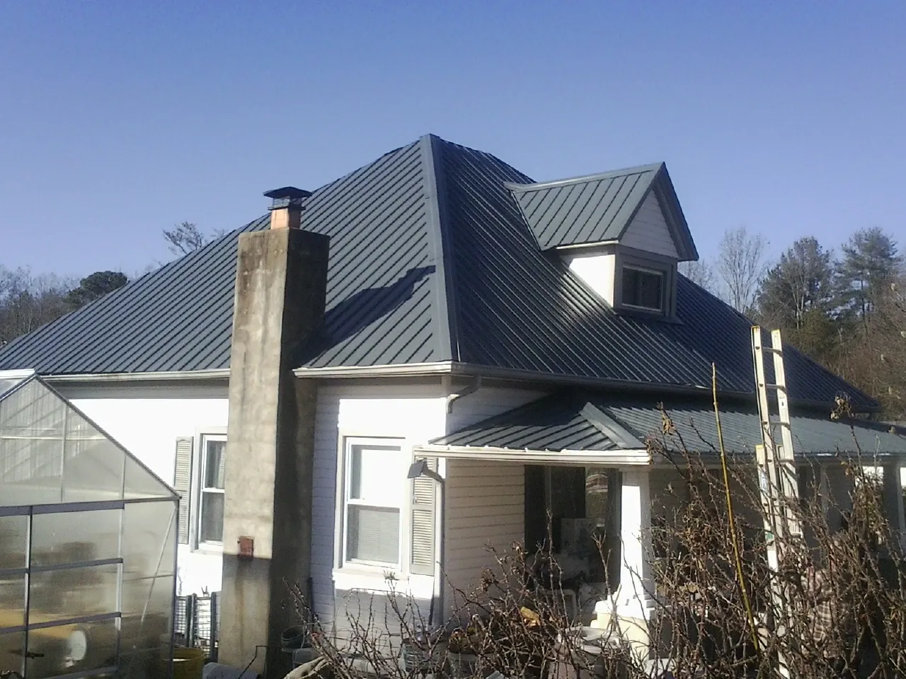 Dark blue standing seam metal roof on a white farmhouse with dormer — Slate & Tile Roof Repair by Roofing Brothers in South Houston