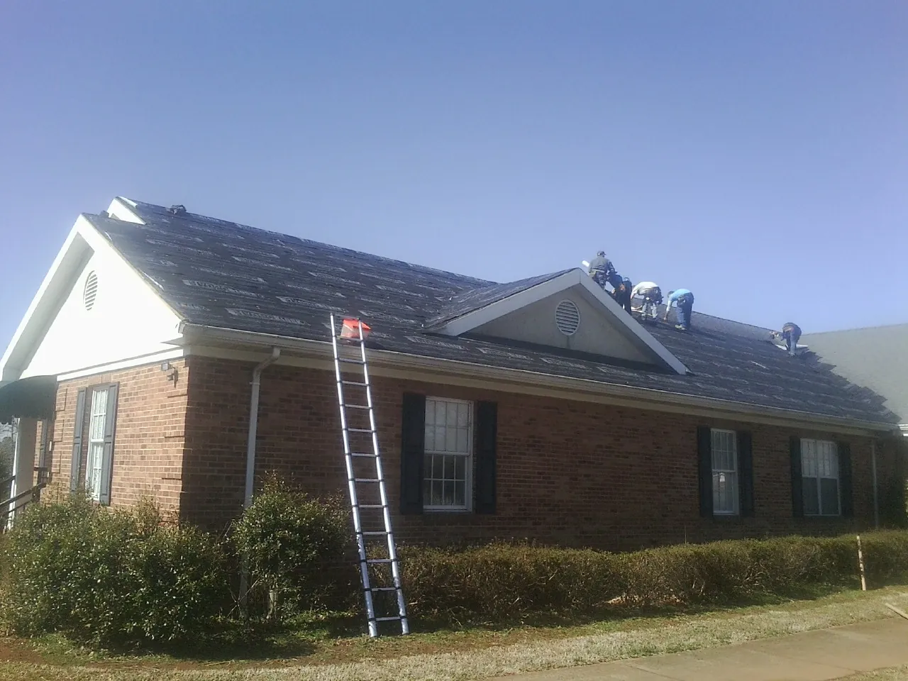 Crew tearing shingles off a brick ranch roof with a ladder set — Metal Roof Repair work by our crew in South Houston