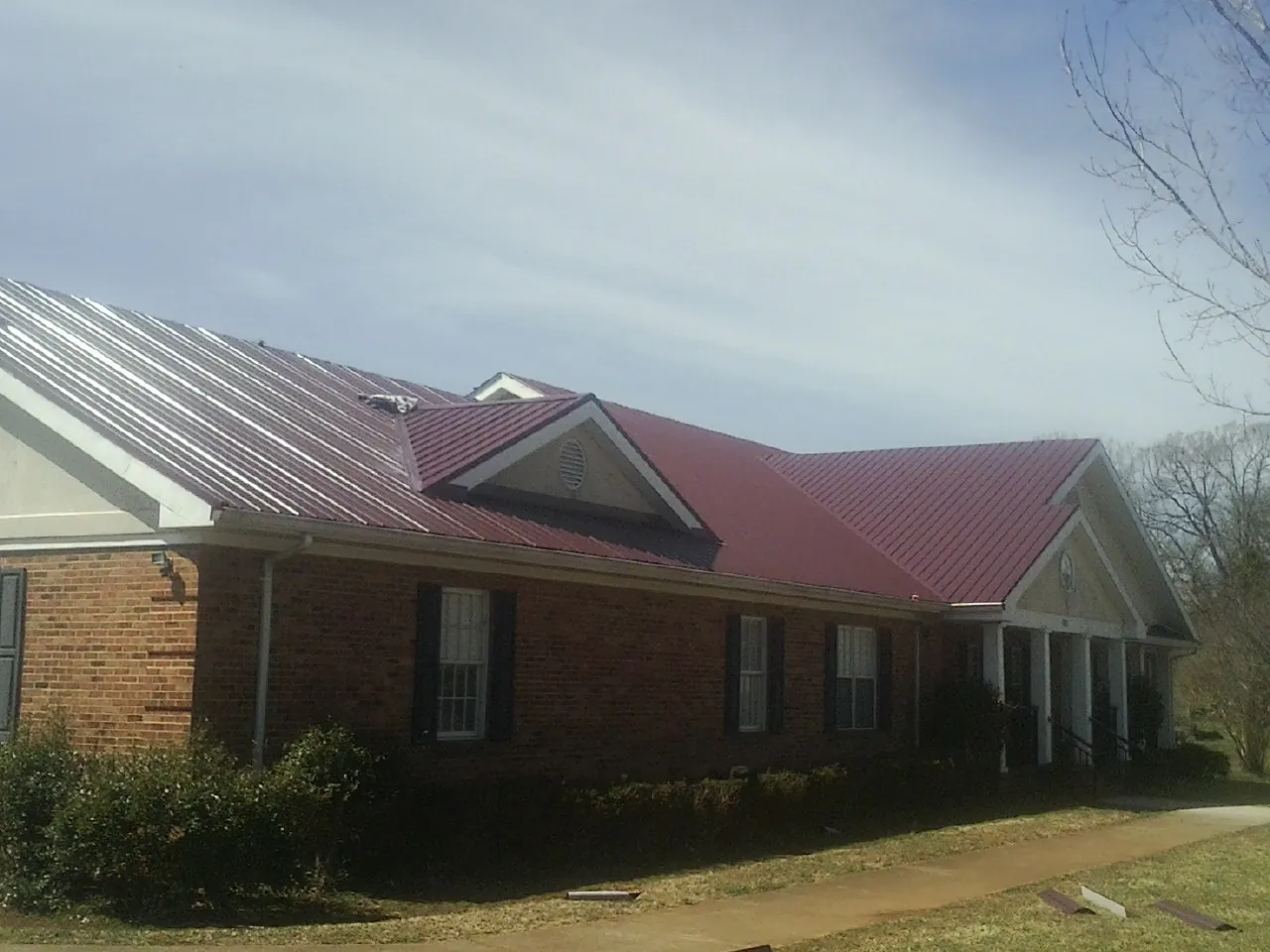 Red metal roof with gabled entries on a long brick building, from a Hail Damage Roof Repair job in South Houston