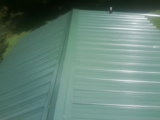 New green metal panels meeting at the ridge of a roof — Flat Roof Repair work by our crew in South Houston