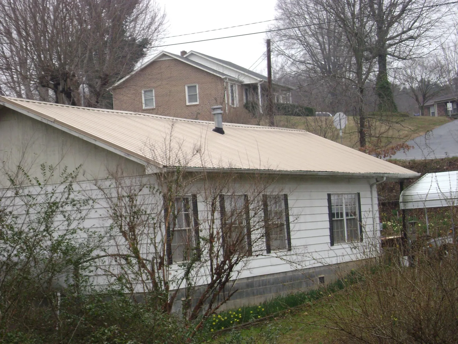Tan metal roof on a white sided house set into a hillside — Commercial Roofing by Roofing Brothers in South Houston